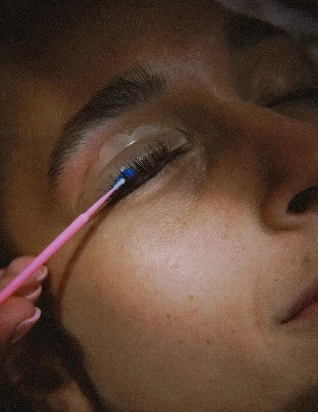 Prestation de réhaussement de cils en cours sur une cliente, application du produit avec un applicateur rose.
