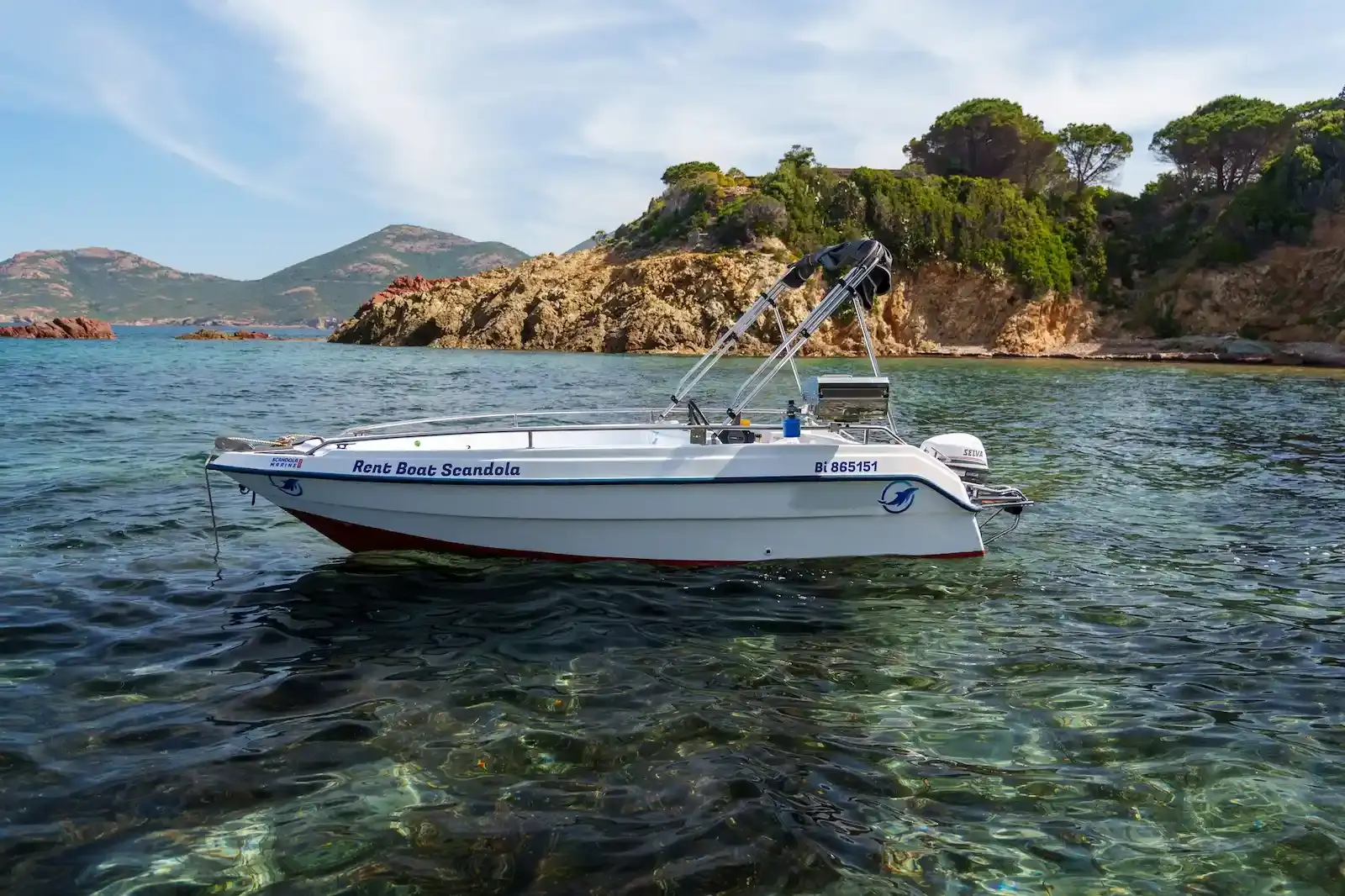 Bateau à moteur de location Scandola Marine au mouillage devant une côte rocheuse sauvage en Haute-Corse.