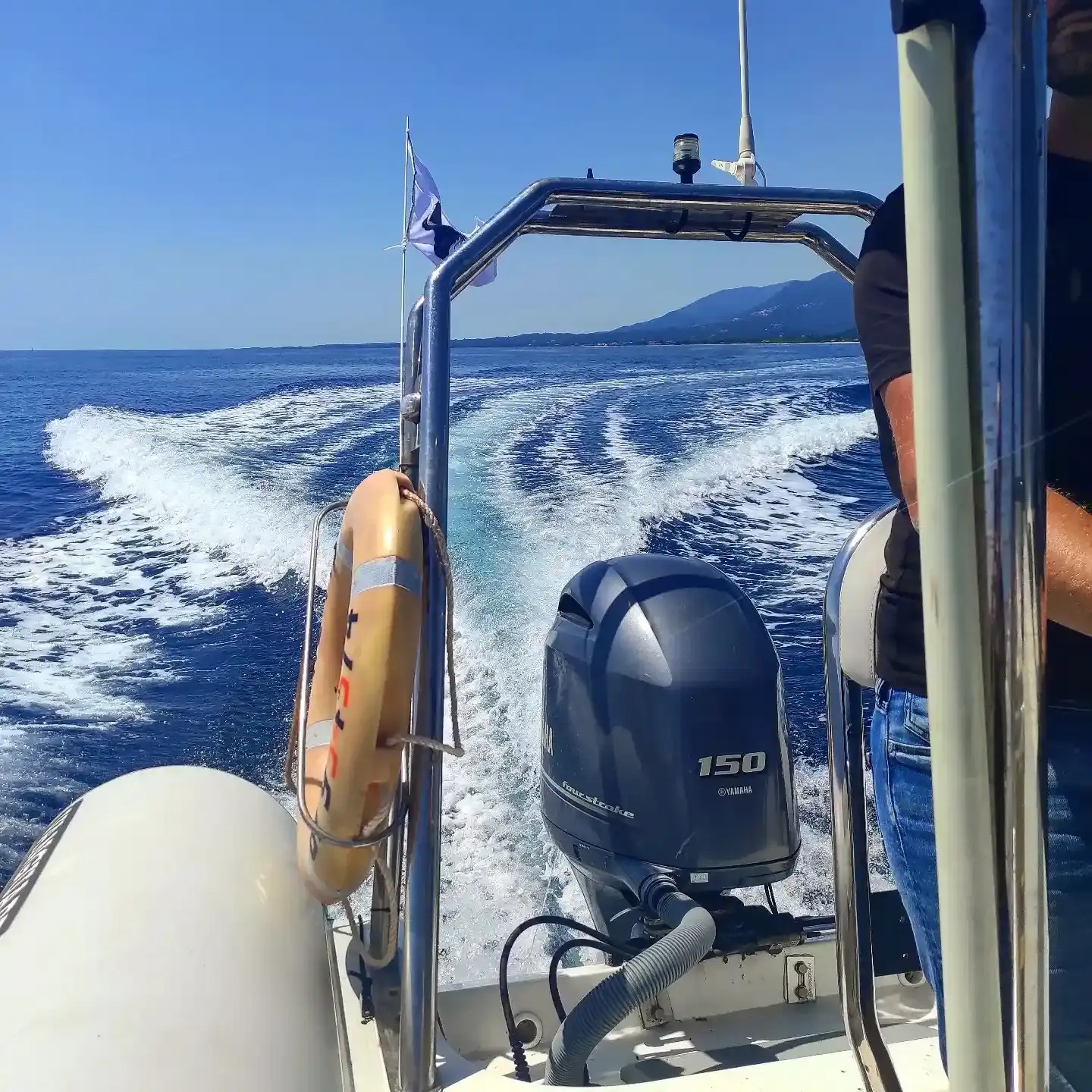 Sillage d'un bateau école en navigation rapide sur une mer calme, avec vue sur le moteur hors-bord Yamaha et les montagnes côtières au loin.