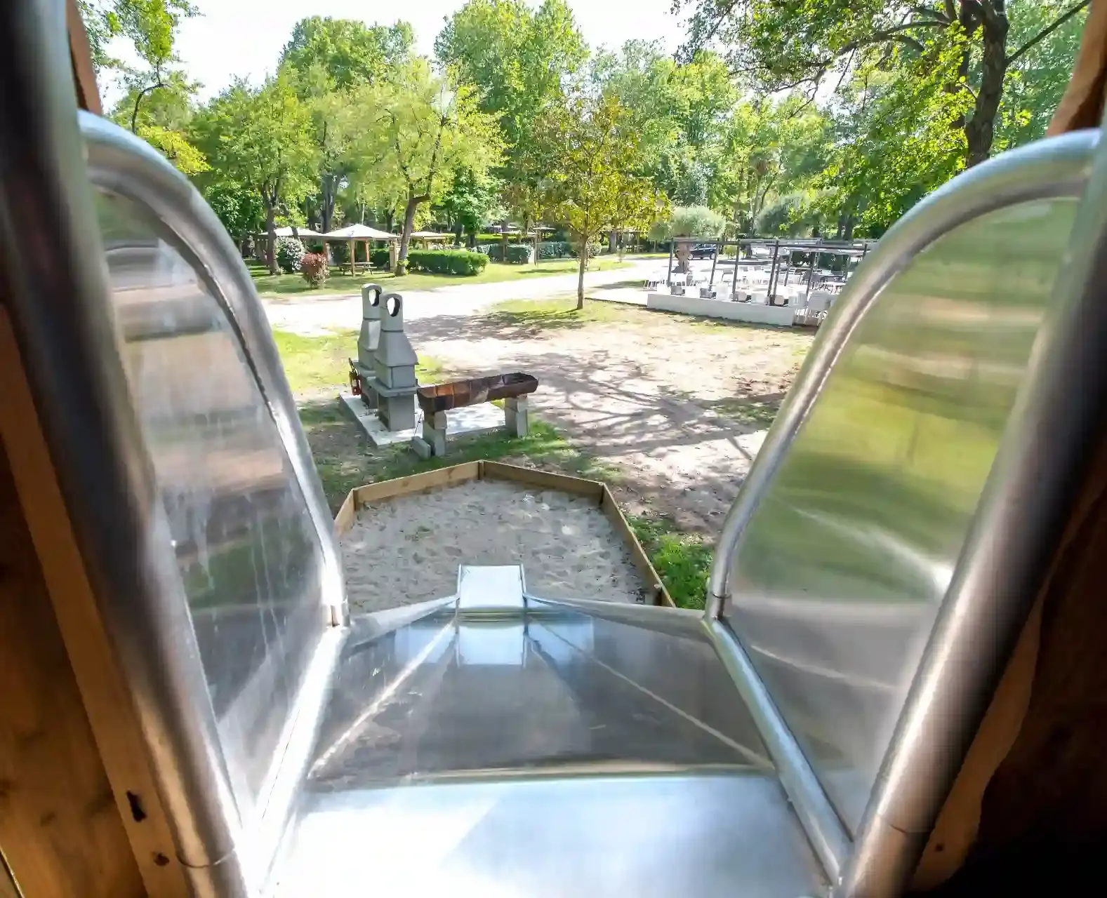 Vue depuis le haut d'un toboggan en inox avec mains courantes sécurisées au Camping Merendella, plongeant vers une zone de réception en sable.