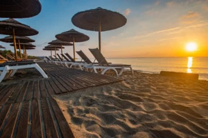 Alignement de transats sous des parasols exotiques en paille sur une plage de sable au coucher du soleil.