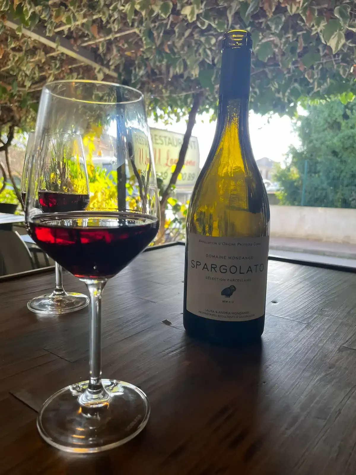 Dégustation de vin rouge AOP Corse Domaine Mondange Spargolato en terrasse ombragée au restaurant U Lampione à Moriani Plage.