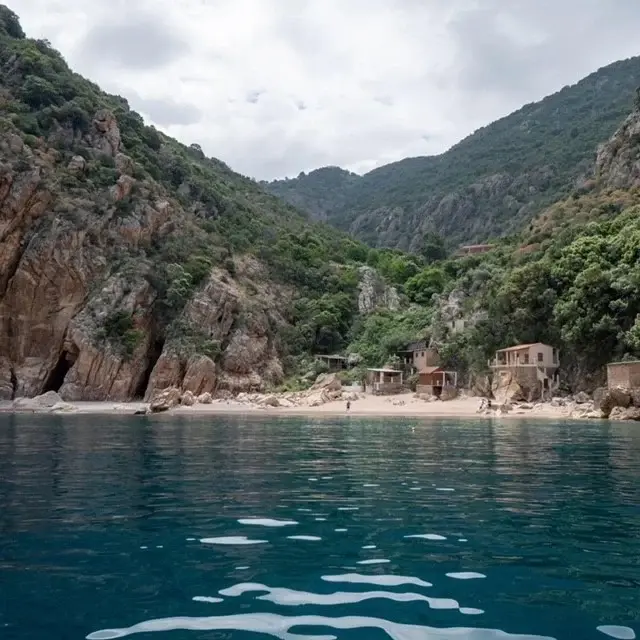 Falaises abruptes et petites maisons de pêcheurs au bord de l'eau dans les Calanques de Piana en Corse, vue depuis la mer.