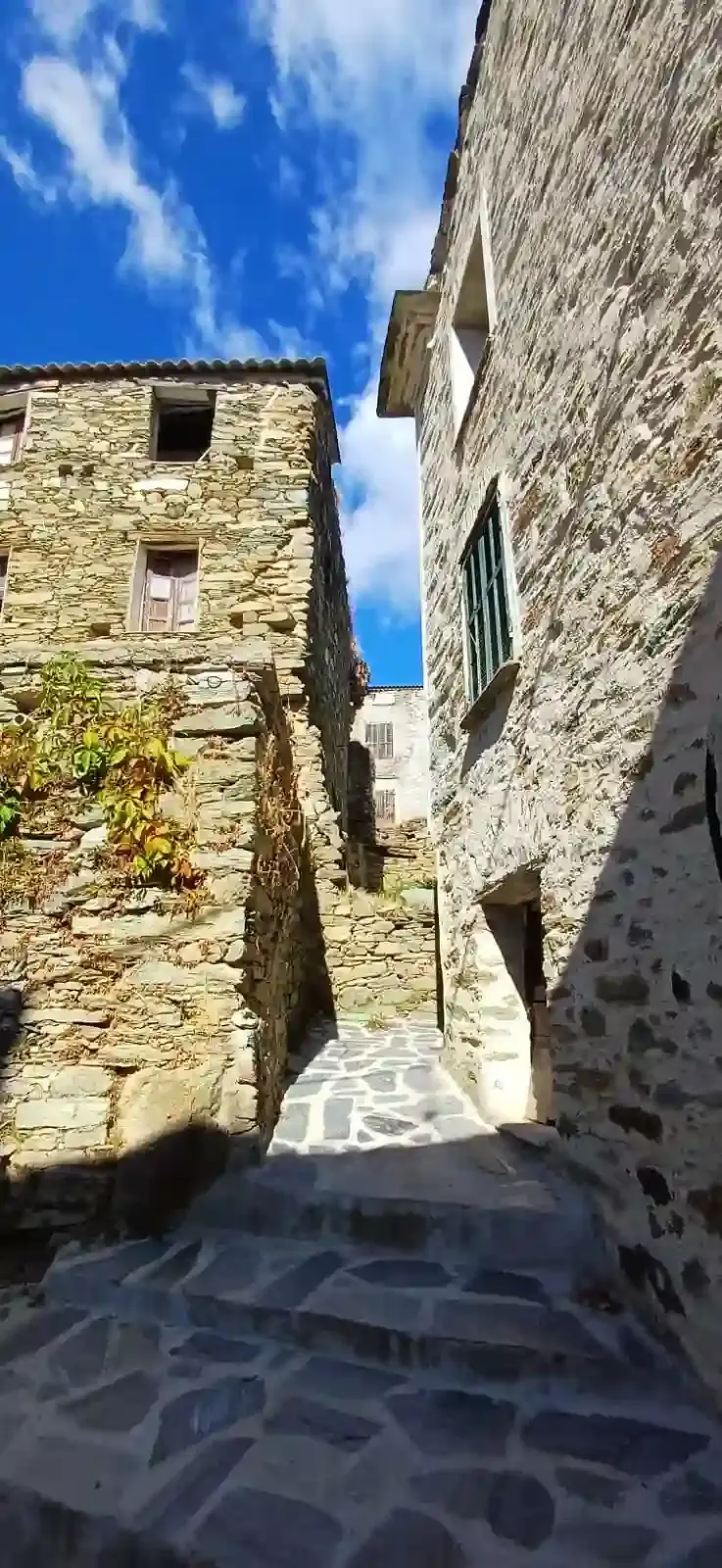 Une ruelle étroite et pavée d'un village corse traditionnel, avec des maisons en pierre et une vue sur le ciel bleu, évoquant l'authenticité de la charcuterie Gozzi. Titre : Ruelle de village corse - Charcuterie Gozzi