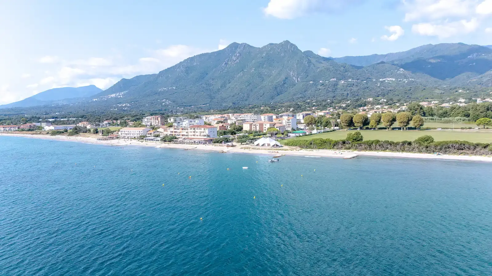 Vue panoramique aérienne de la station balnéaire de Moriani-Plage en Haute-Corse, montrant le front de mer, les résidences de vacances et les montagnes de la Castagniccia surplombant la Costa Verde.
