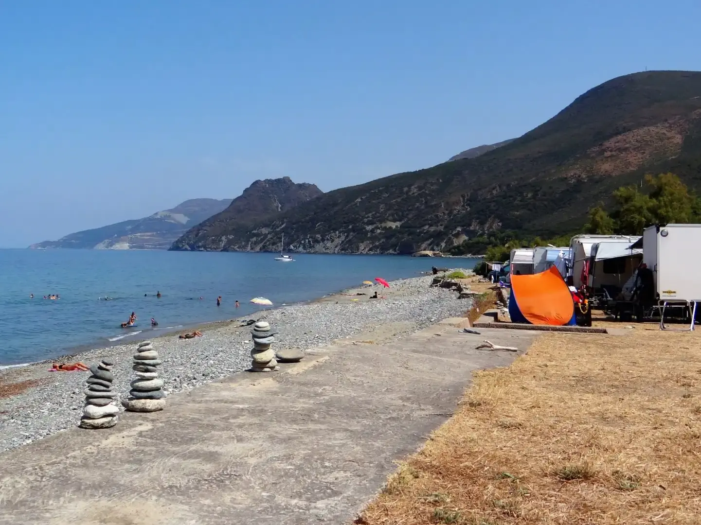Sentier sablonneux menant directement à une plage de galets et d'eau turquoise en Haute-Corse.
