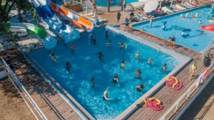 Vue aérienne d'un grand parc aquatique en Haute-Corse avec plusieurs piscines, des toboggans géants colorés et des vacanciers se relaxant sur des transats.