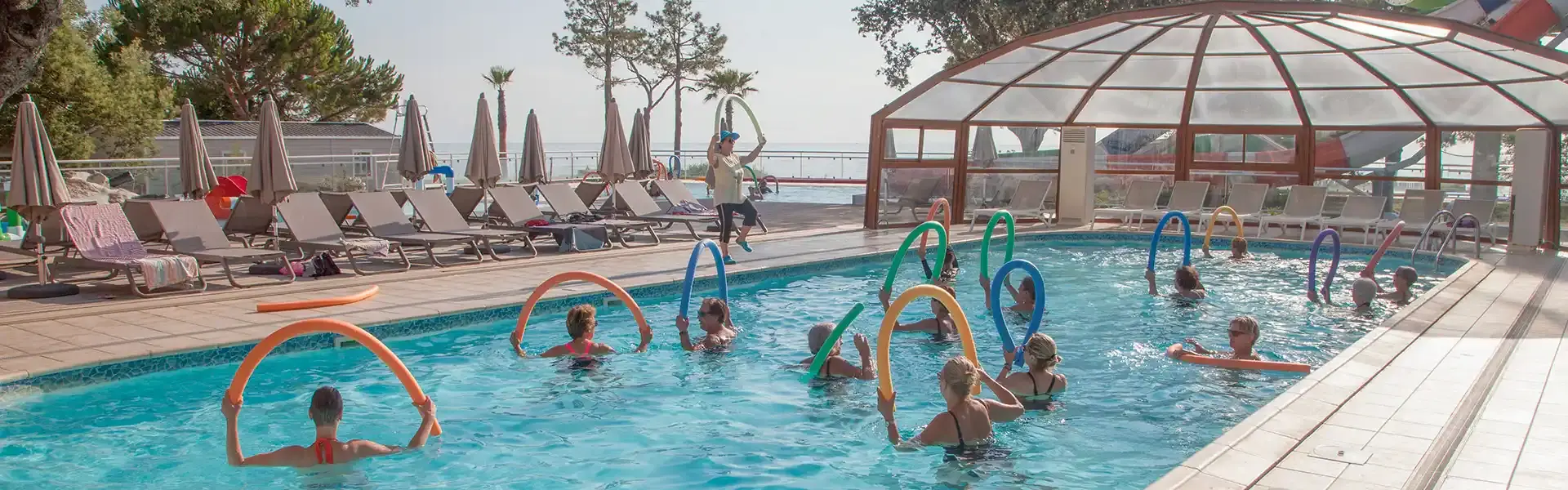 Groupe de participants pratiquant une séance d'aquagym dynamique avec des frites en mousse dans une piscine extérieure ensoleillée.