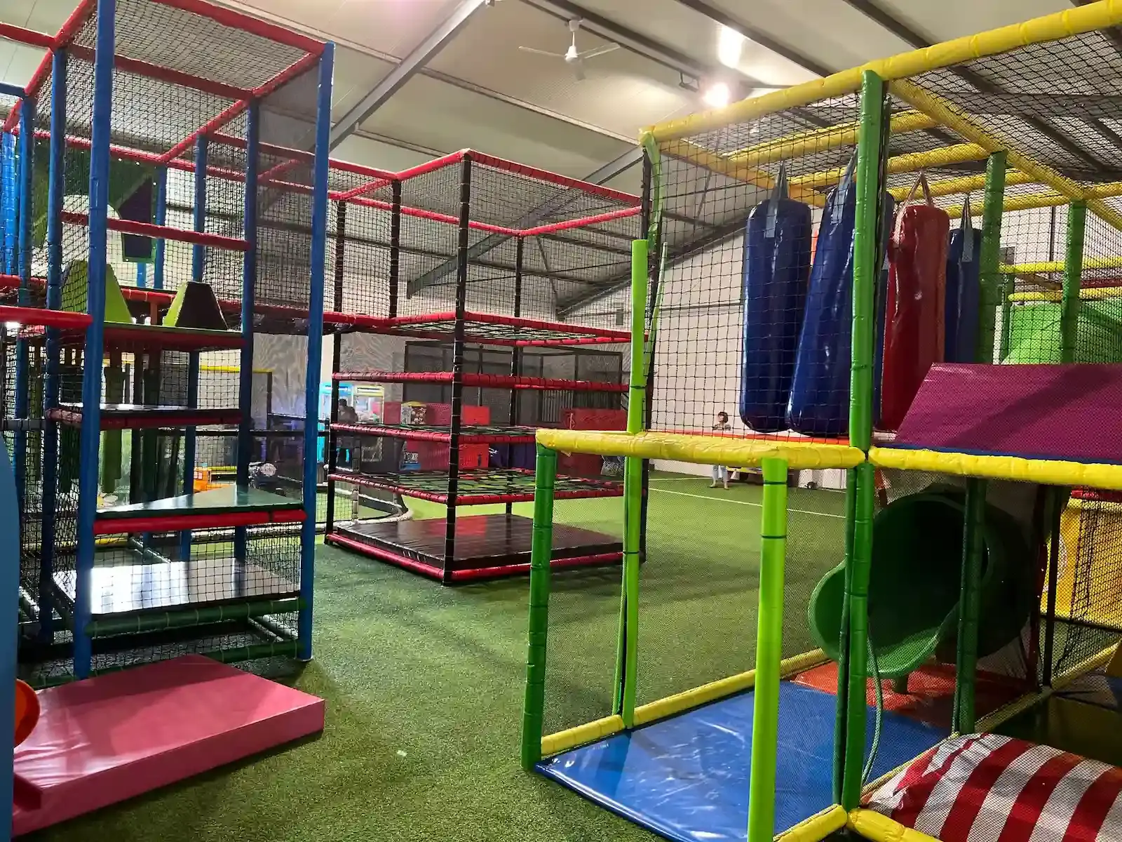 Parc de jeux intérieur avec structures tubulaires colorées, filets de protection et sacs de frappe au Family Parc de Biguglia.
