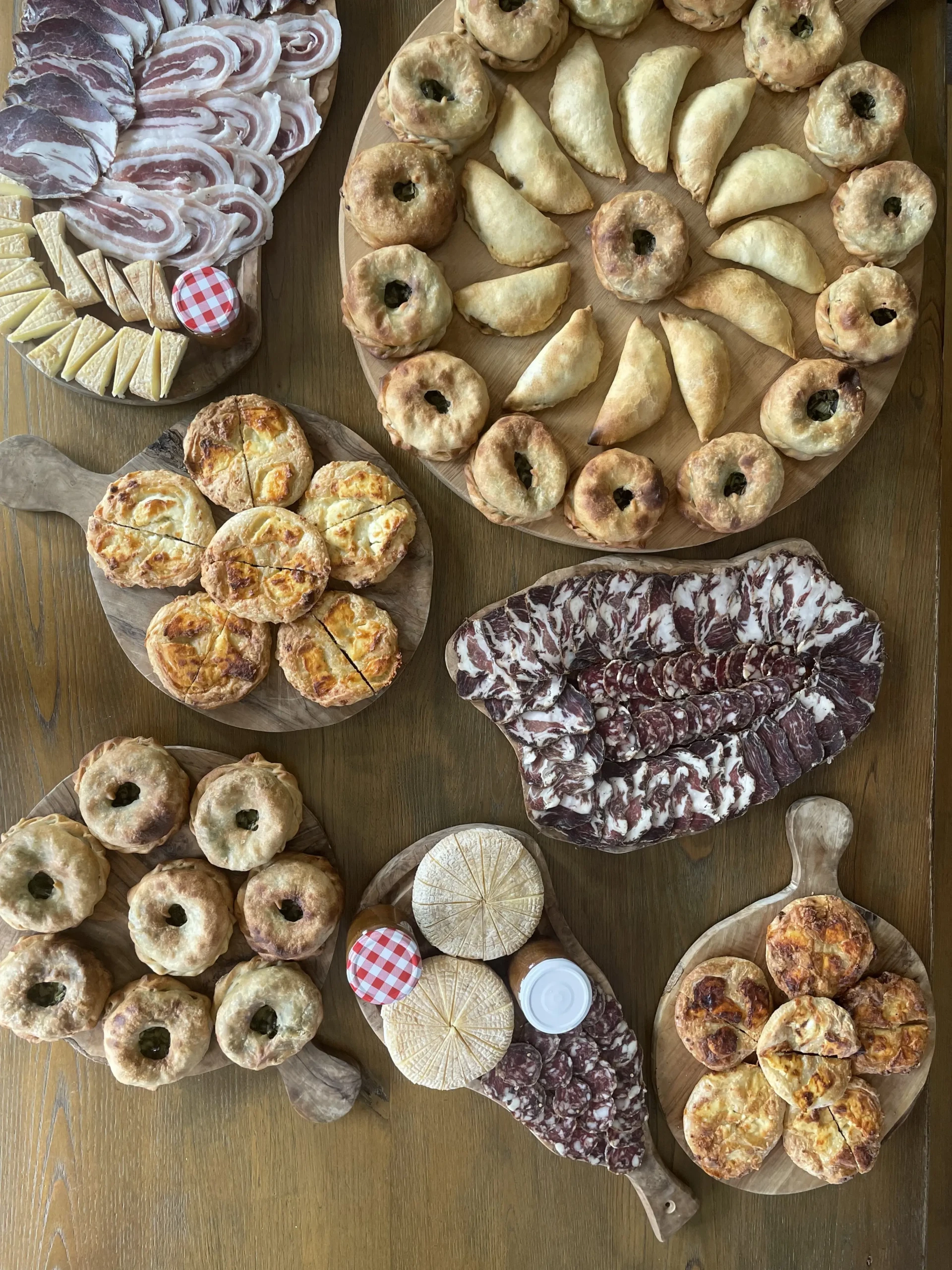 Assortiment de spécialités corses sur des planches en bois avec charcuterie artisanale, beignets au brocciu, fromages ronds et terrines.