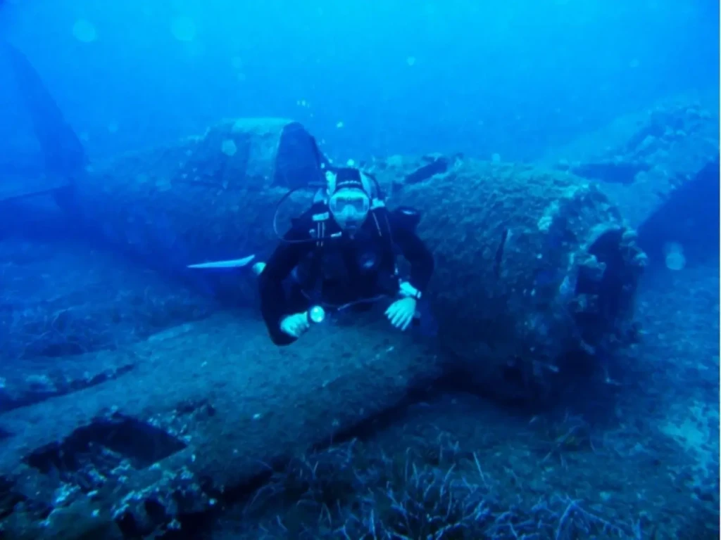 club-plongee-bastiais-haute-corse Un plongeur équipé d'une lampe explore l'épave d'un avion de chasse P-47 Thunderbolt posée sur le sable en Haute-Corse.