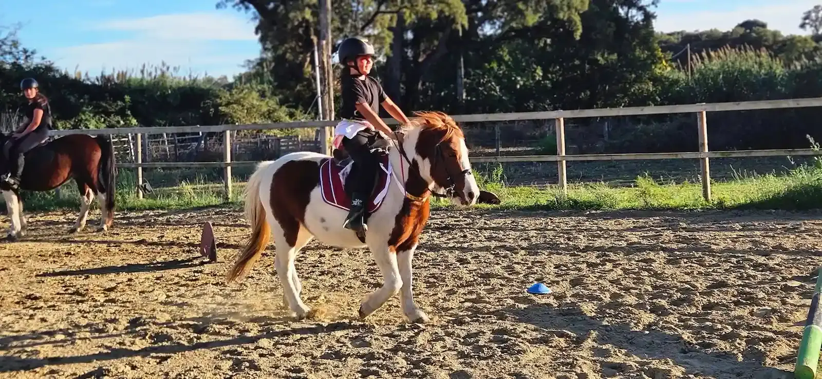 Jeune cavalier équipé d'une bombe montant un poney pie (marron et blanc) au trot dans la carrière du club de San Giuliano.