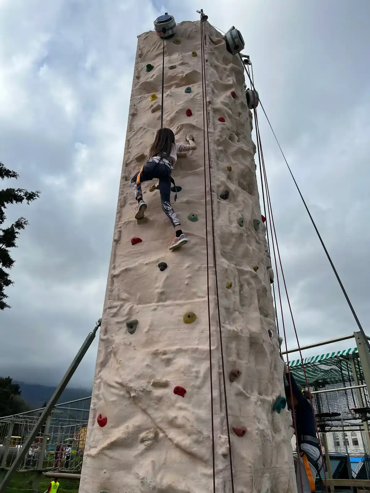 Jeune fille grimpant sur un mur d'escalade extérieur sécurisé avec harnais au Family Parc en Haute-Corse.