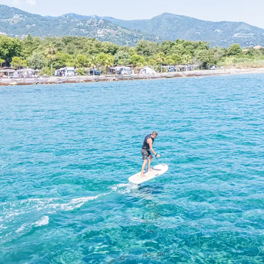 Homme en équilibre sur une planche de surf électrique e-foil volant au-dessus des eaux turquoise de la Côte Orientale corse.