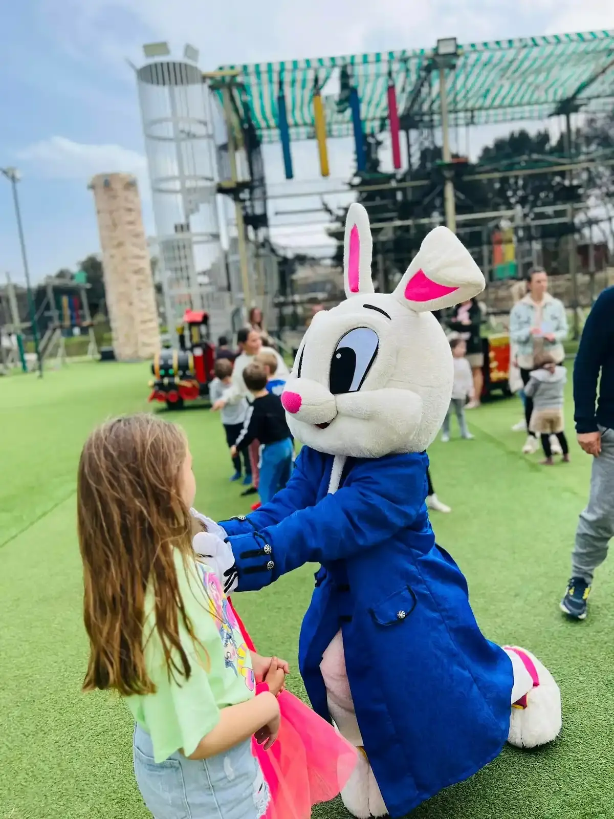 Mascotte de lapin blanc en costume bleu interagissant avec une petite fille sur la pelouse du Family Parc.