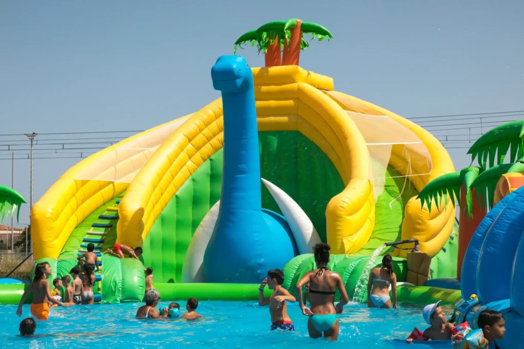 Children playing in a pool with a blue dinosaur-shaped inflatable slide at Family Parc in Corsica.