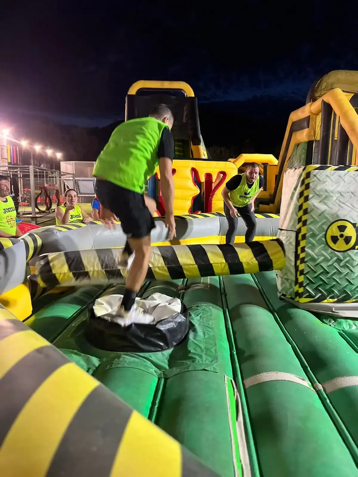 Adultes portant des dossards fluo participant à un parcours d'obstacles gonflable "Meltdown" de nuit au Family Parc.