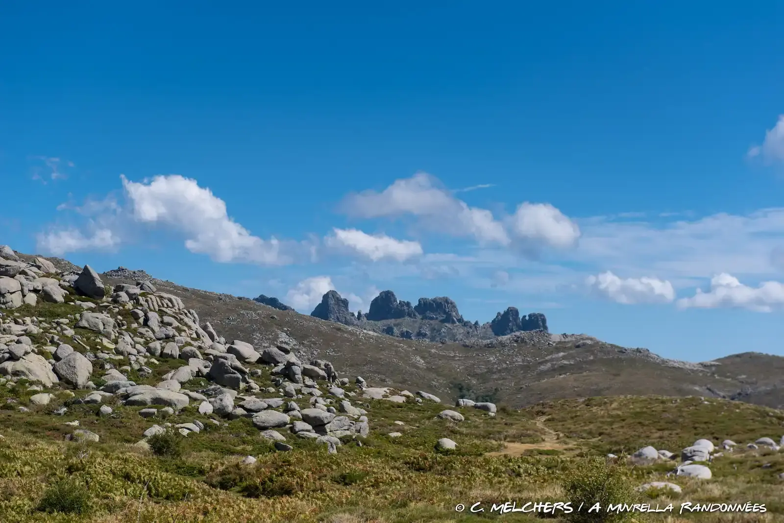 Crêtes de montagnes rocheuses et pointues se découpant sur un ciel parsemé de nuages blancs.