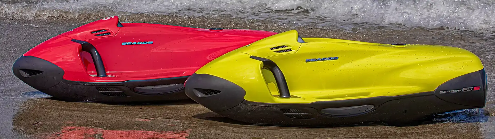 Deux engins de propulsion sous-marine Seabob, l'un rouge et l'un jaune, posés sur le bord de l'eau.