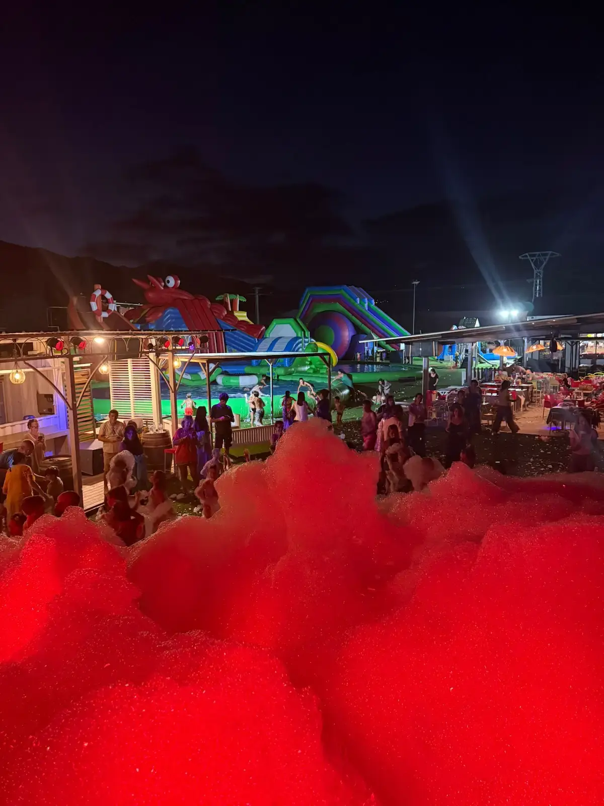 Vue nocturne d'une soirée mousse avec éclairage rouge intense et structures gonflables lumineuses au Family Parc en Corse.