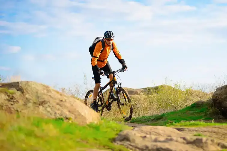 vtt-haute-corse Cycliste équipé d'un casque et d'un sac à dos roulant sur un chemin escarpé de Haute-Corse sous un ciel bleu.